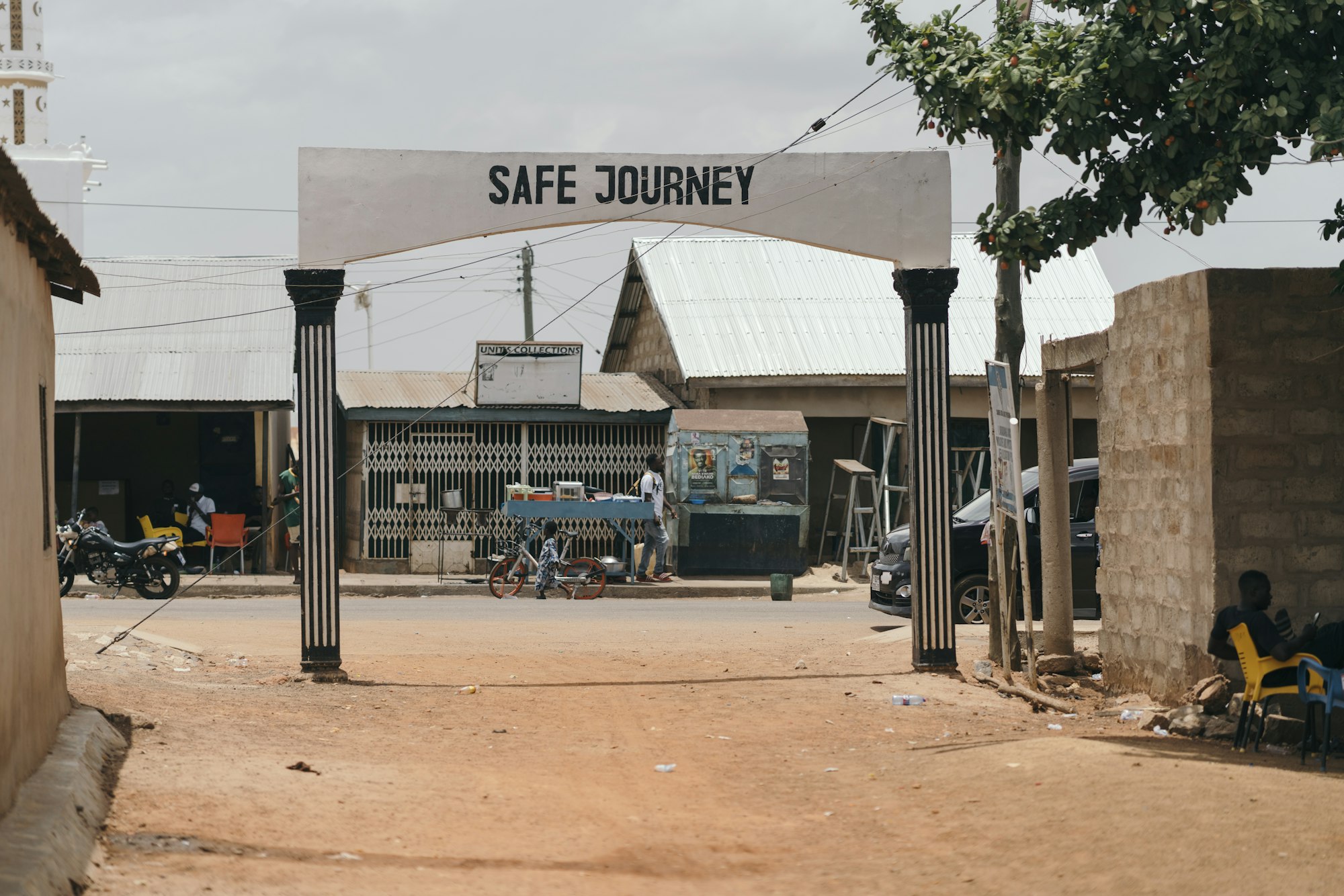 Rue commerçante d’une ville ouest-africaine : échoppes, étal mobile et deux-roues sous un portique.