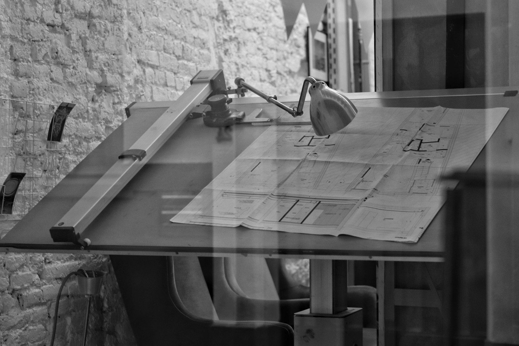Table à dessin d’architecte : plans dépliés, règle parallèle et lampe d’atelier.