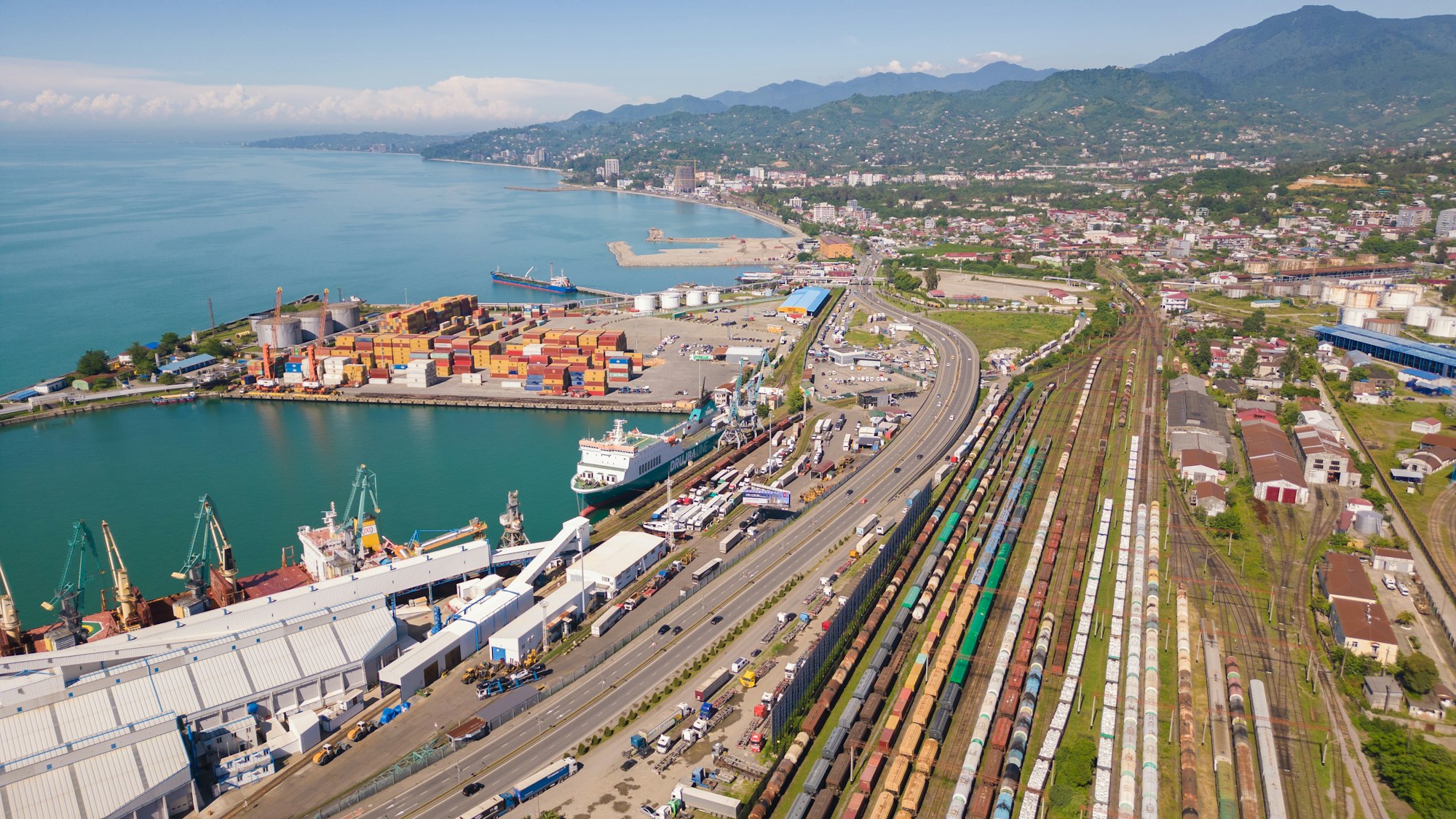 Terminal portuaire vu du ciel : conteneurs empilés, portiques, faisceau ferroviaire et voie rapide.